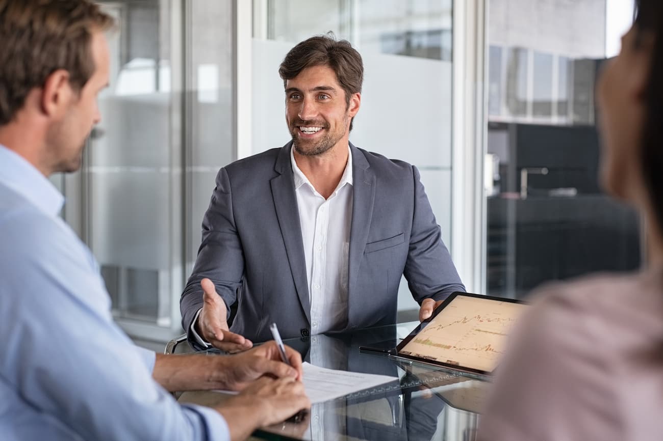 Geschäftsmann präsentiert einem Team in einem modernen Büro einen Bericht auf einem Tablet, symbolisiert die Analyse der Testergebnisse und die Erstellung eines klaren Reports mit Handlungsempfehlungen.