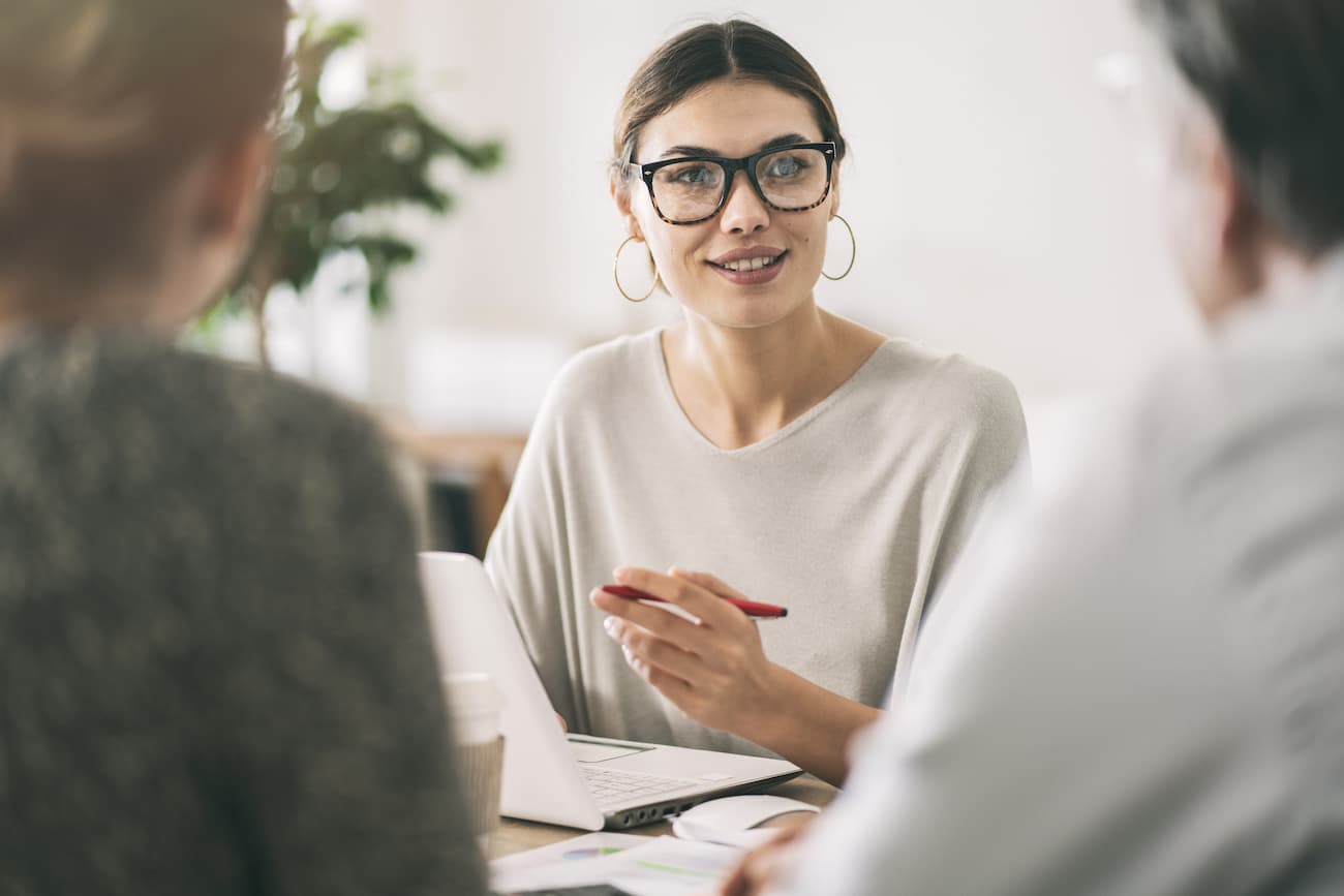 Frau mit Brille diskutiert mit Kollegen in einem Büro, symbolisiert die Entwicklung qualitativ hochwertiger Fragebögen und die Durchführung von Befragungen während des gesamten Produktlebenszyklus.