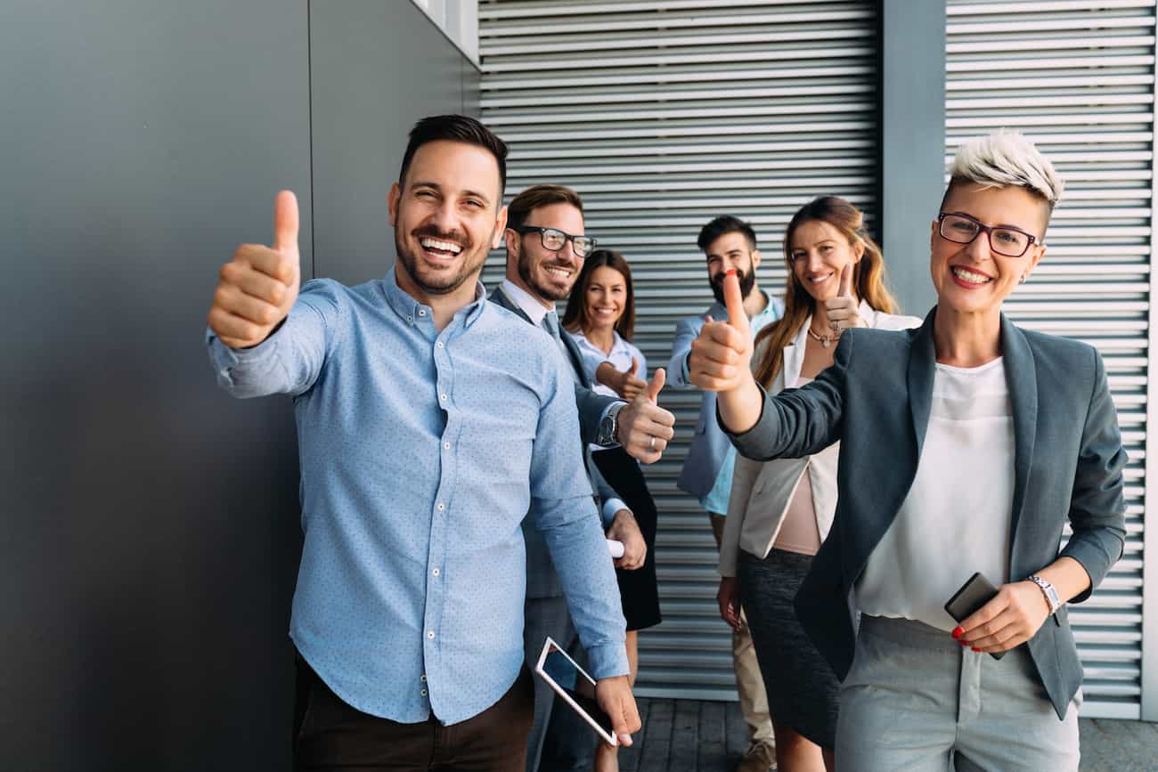 Fröhliches Team von Fachkräften gibt Daumen hoch, symbolisiert die Anforderungen und den Enthusiasmus, um als Crowdtester/in erfolgreich durchzustarten.