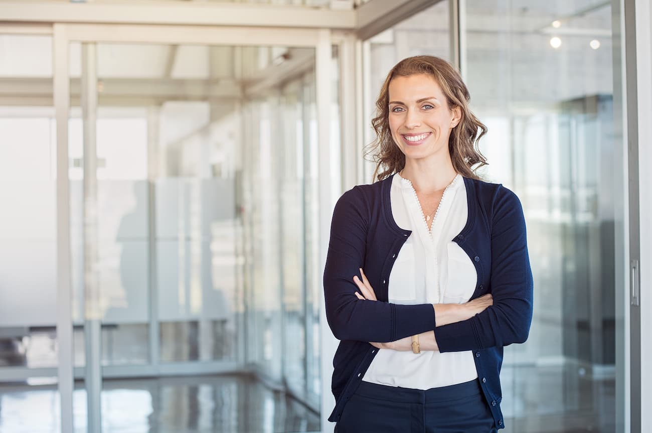 Eine selbstbewusste Geschäftsfrau in einem modernen Bürogebäude, die mit verschränkten Armen lächelt, symbolisiert die Erfahrung und kundenzentrierte Expertise von passbrains.