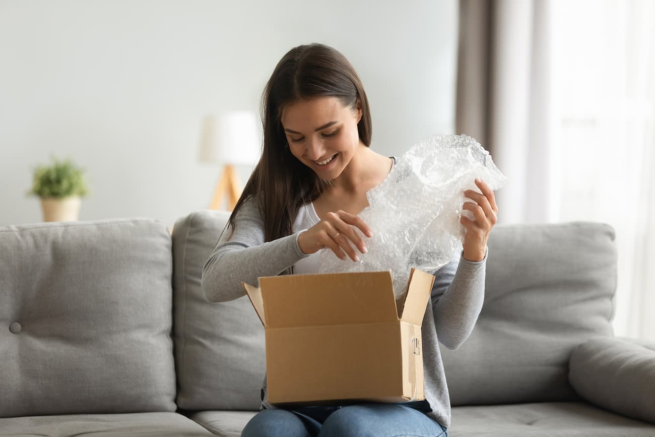 Frau öffnet eine Verpackung auf einem Sofa, symbolisiert das Einkaufserlebnis beim Mystery Shopping.