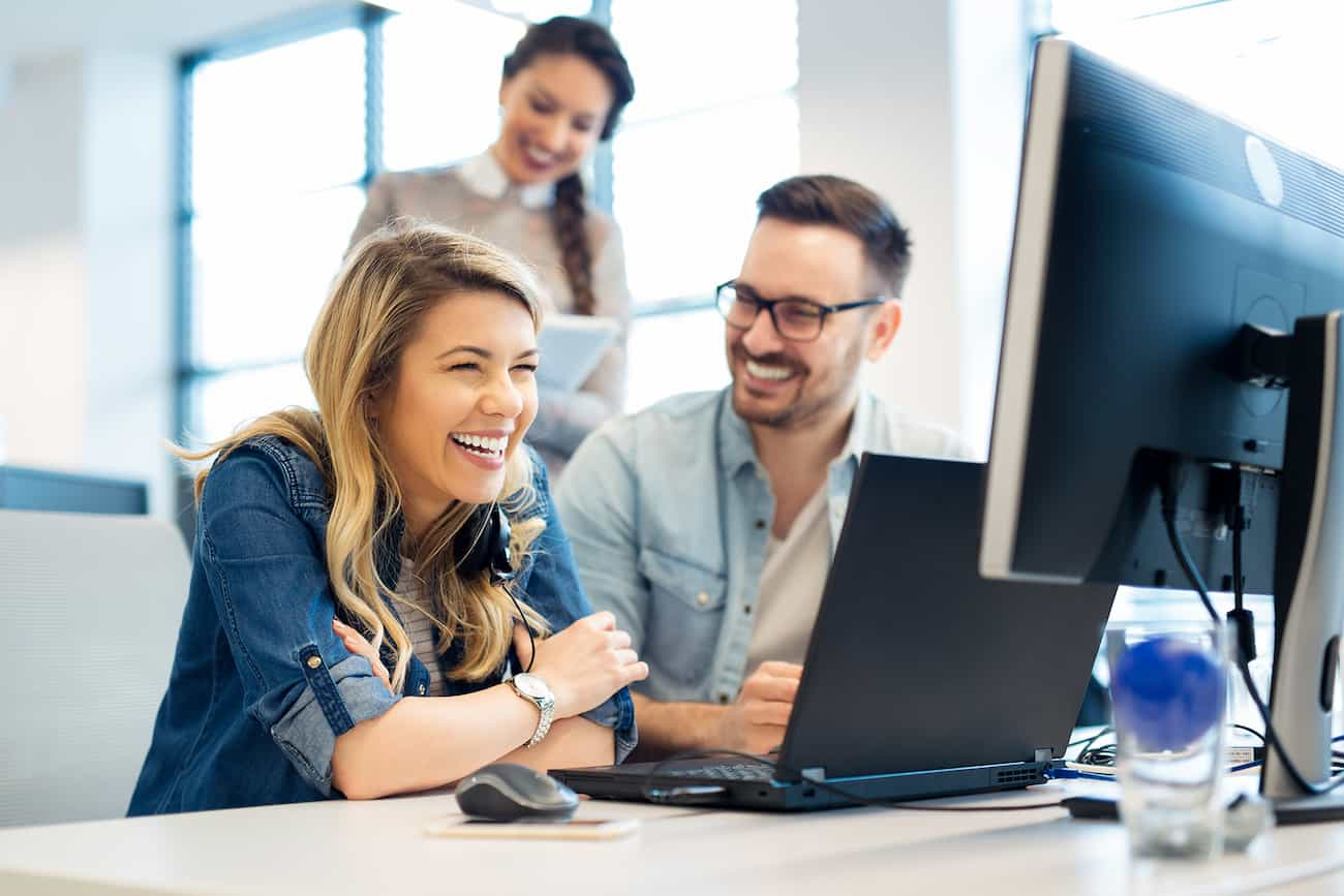 Lächelnde Teammitglieder diskutieren zusammen vor einem Computerbildschirm in einem modernen Büro.